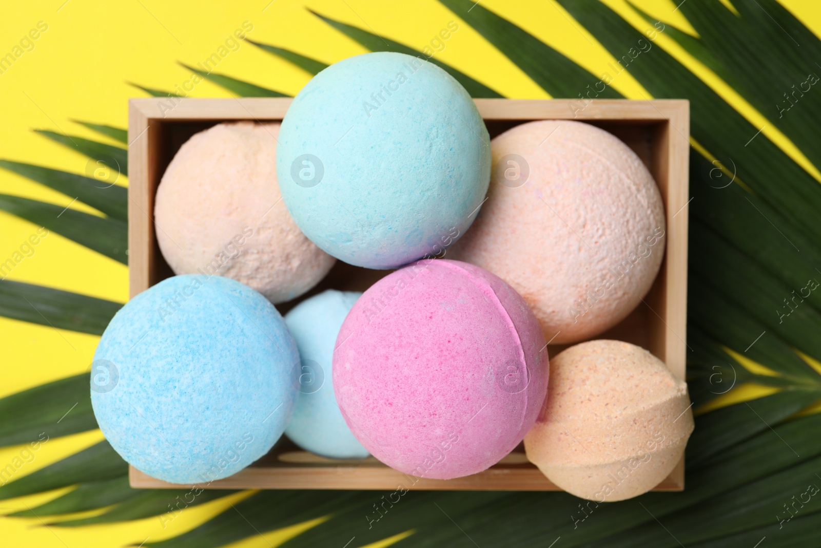 Photo of Wooden crate with bath bombs and green leaf on yellow background, flat lay