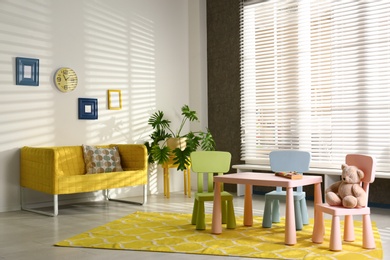 Photo of Stylish playroom interior with table, chairs and sofa