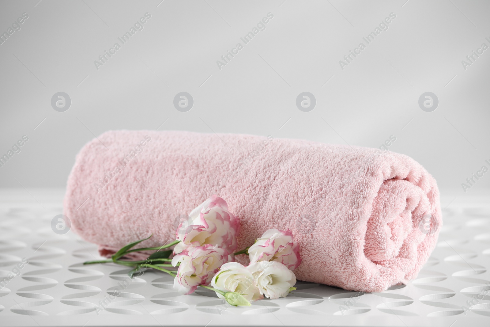 Photo of Rolled soft towel and eustoma flowers on white table