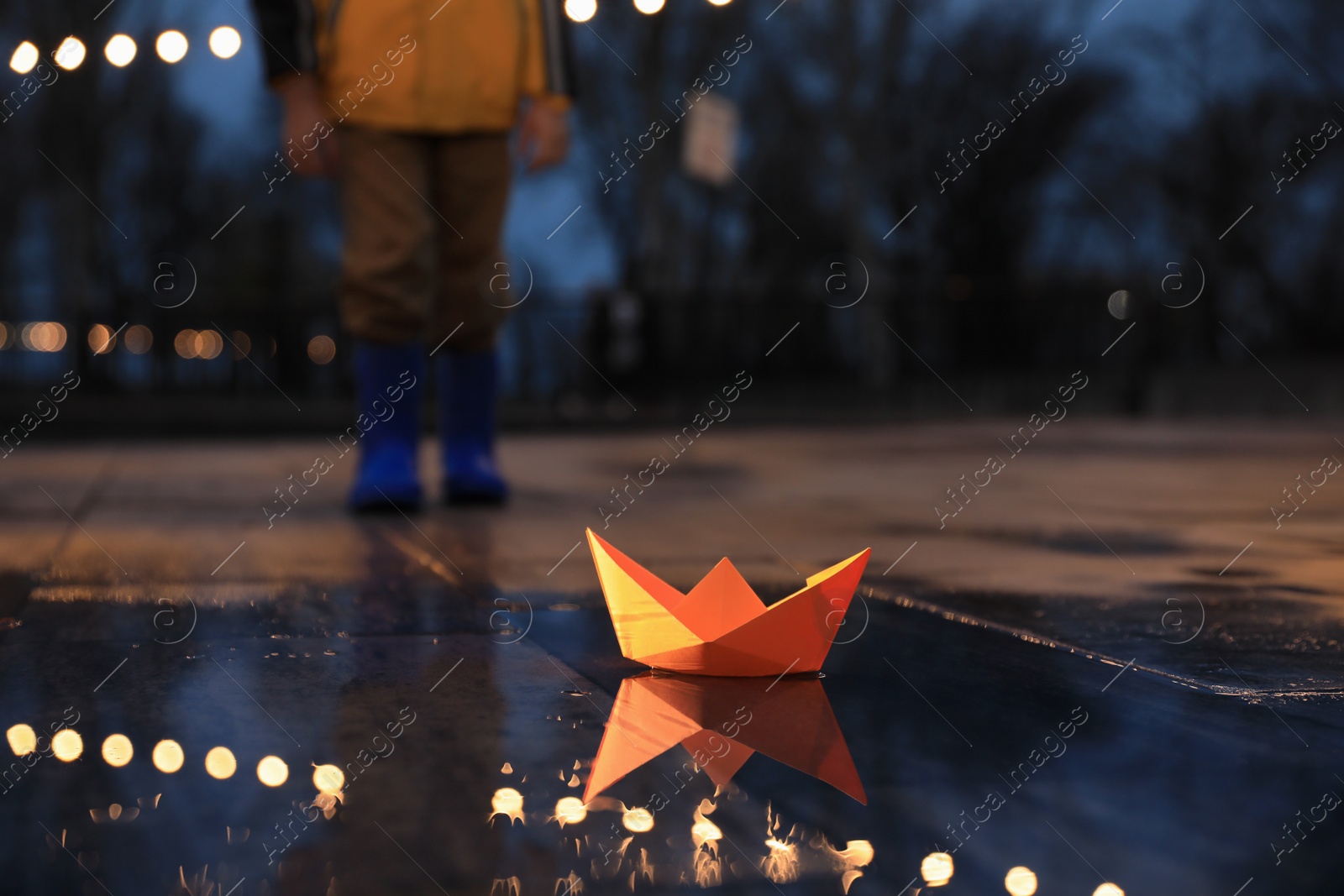 Photo of Little boy outdoors, focus on paper boat in puddle