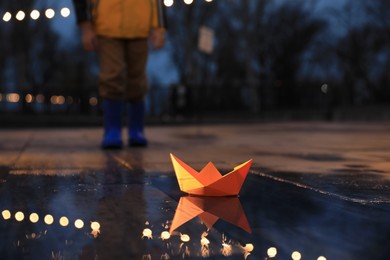 Photo of Little boy outdoors, focus on paper boat in puddle