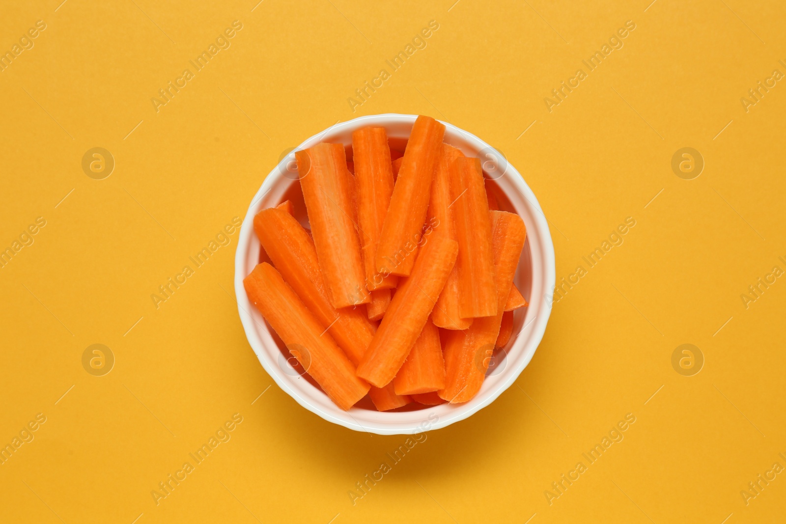 Photo of Cut fresh carrot in bowl on orange background, top view. Finger food