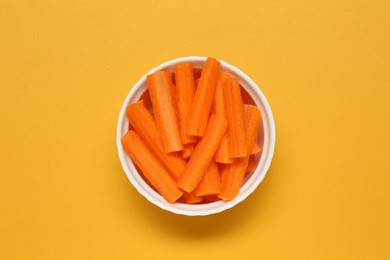 Cut fresh carrot in bowl on orange background, top view. Finger food