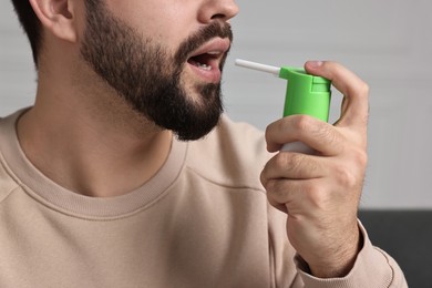 Photo of Young man using throat spray indoors, closeup