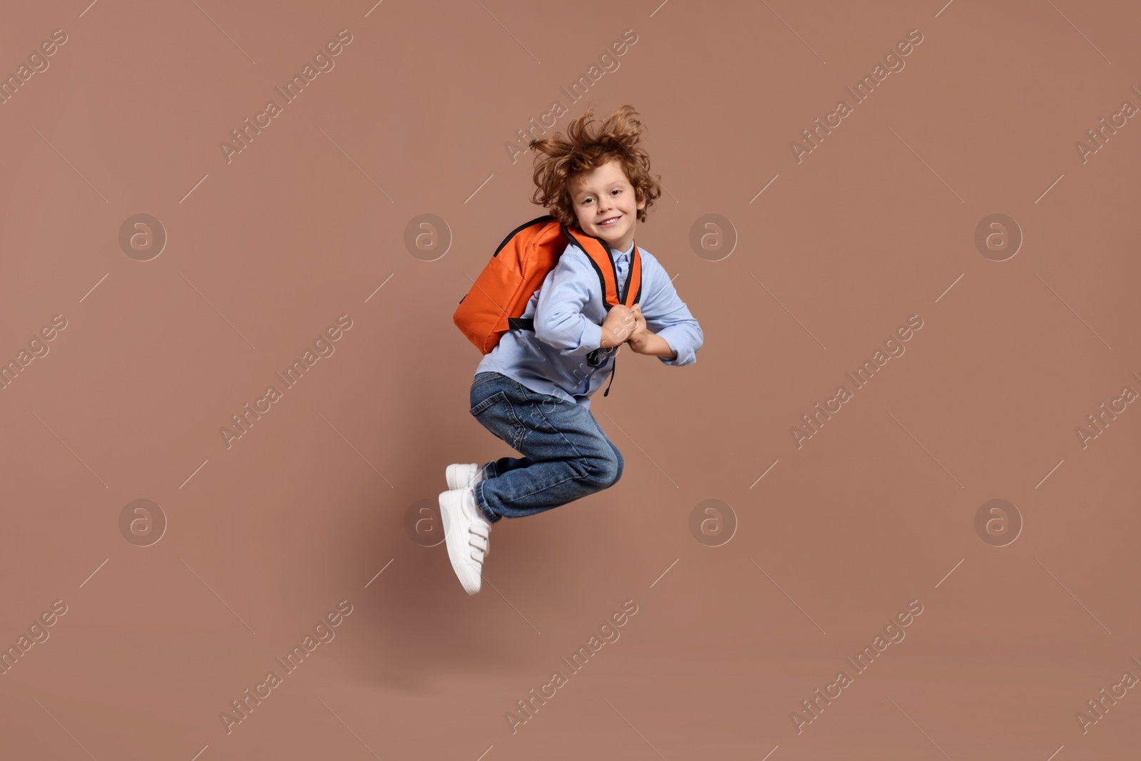 Photo of Happy schoolboy with backpack jumping on brown background