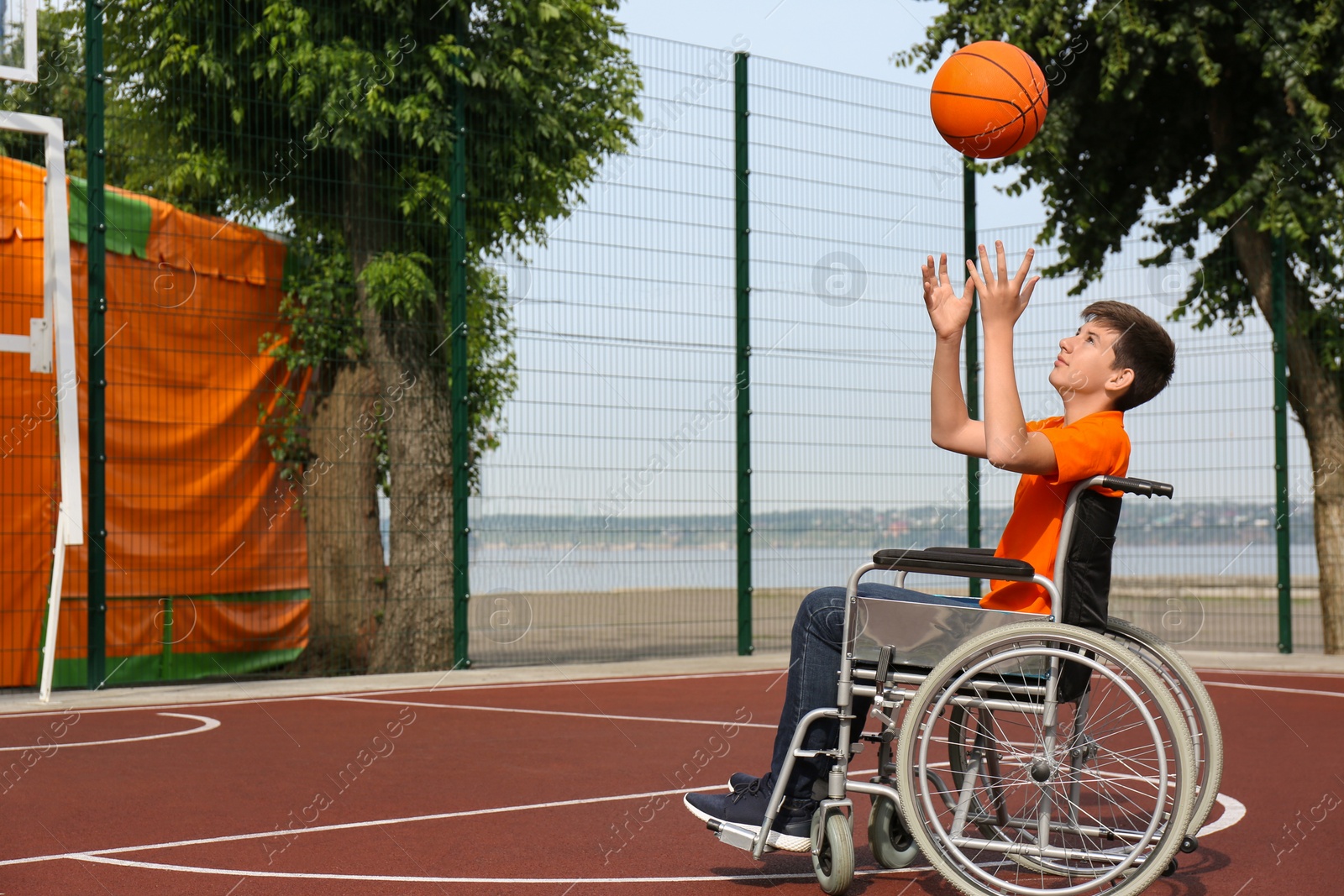 Photo of Disabled teenage boy in wheelchair playing basketball  on outdoor court