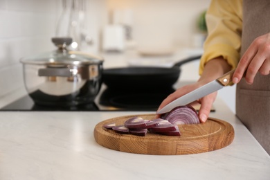 Photo of Woman cutting red onion into slices at table in kitchen, closeup