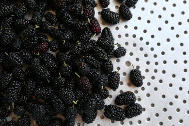 Photo of Heap of delicious ripe black mulberries in colander, top view