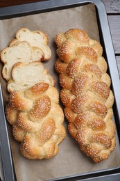 Photo of Baking tray with homemade braided bread on wooden table, top view. Traditional Shabbat challah