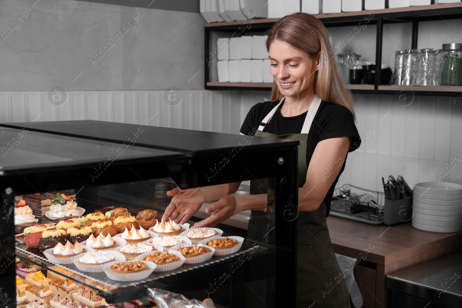 Photo of Happy seller taking delicious dessert from showcase in bakery shop