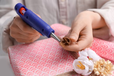 Photo of Woman using hot glue gun to decorate gift at white table, closeup