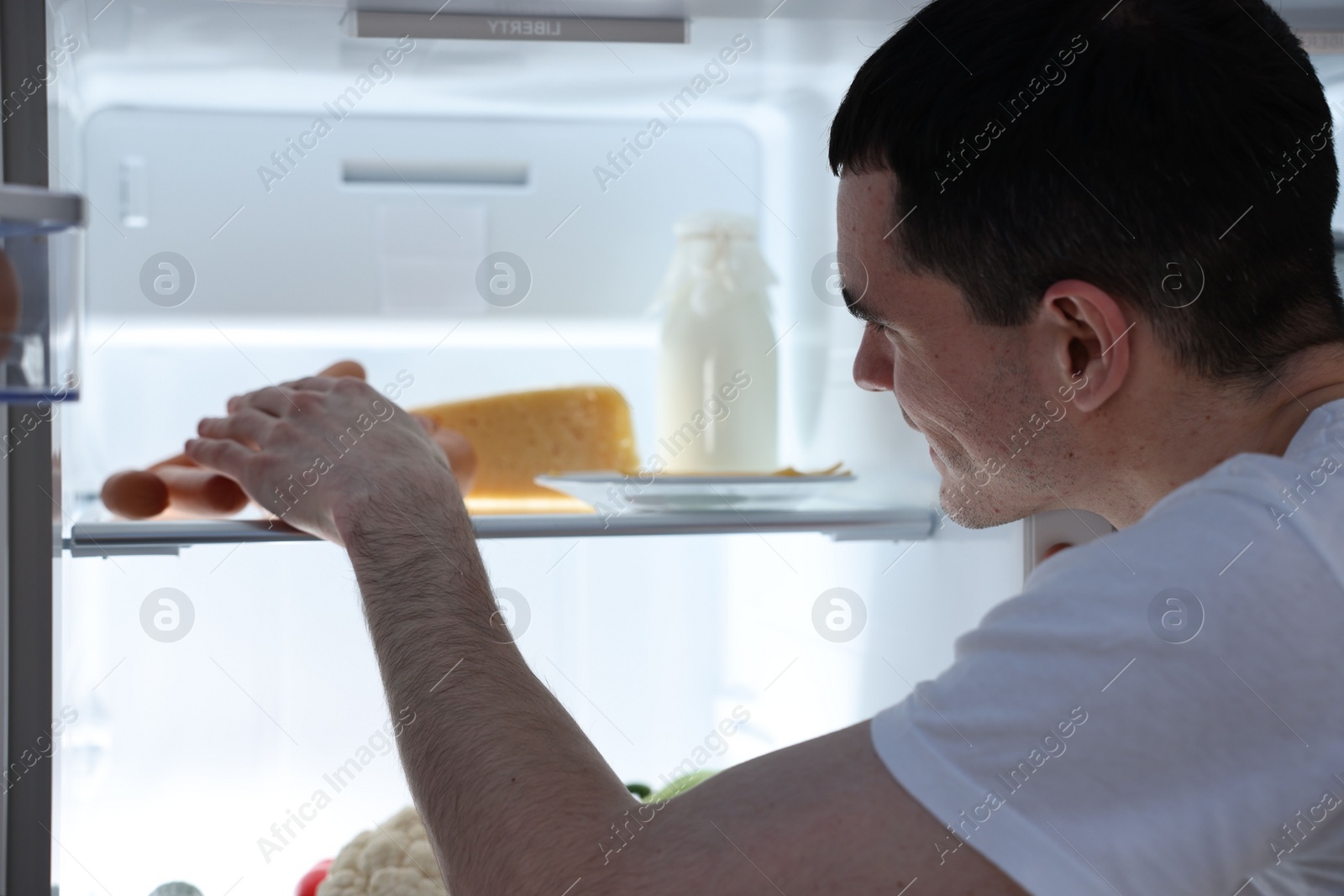 Photo of Man taking sausages out of refrigerator at night