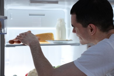 Man taking sausages out of refrigerator at night