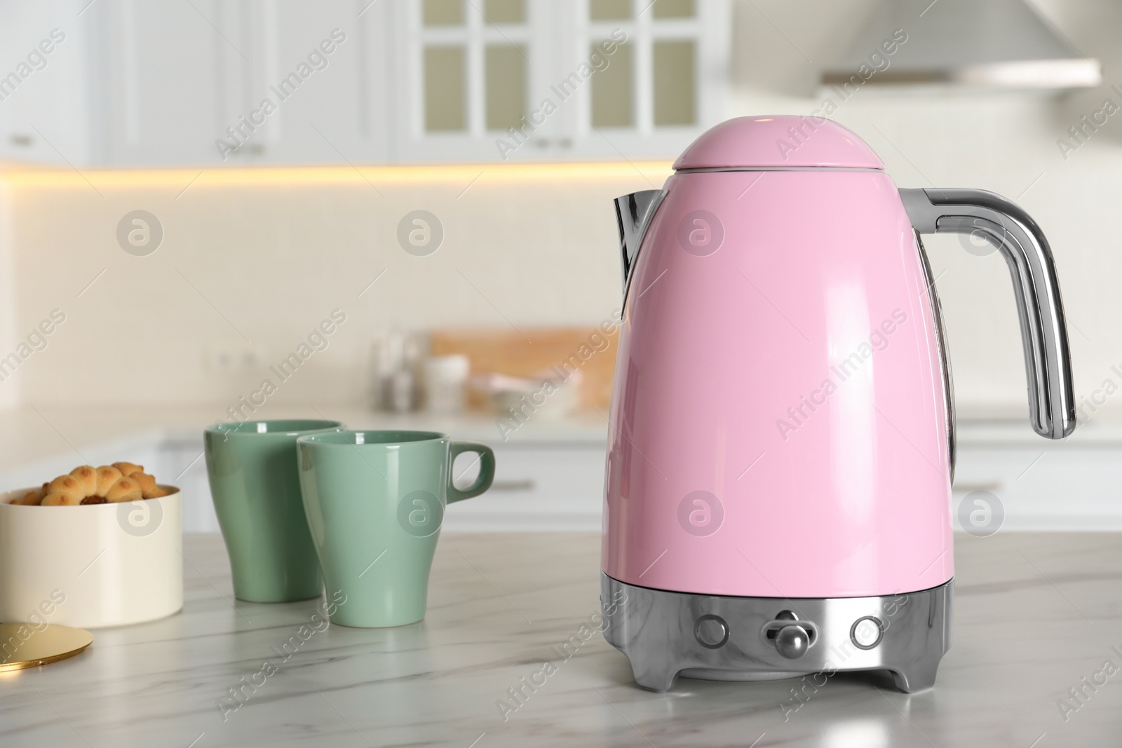 Photo of Modern electric kettle, cups and cookies on table in kitchen