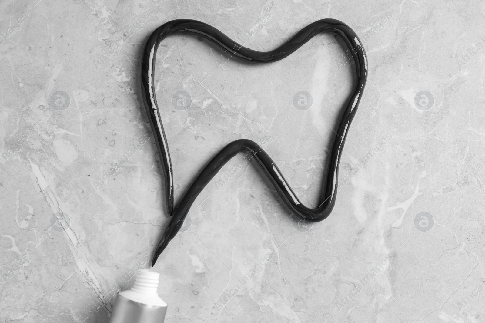 Photo of Tooth drawn with charcoal toothpaste on light grey table, flat lay