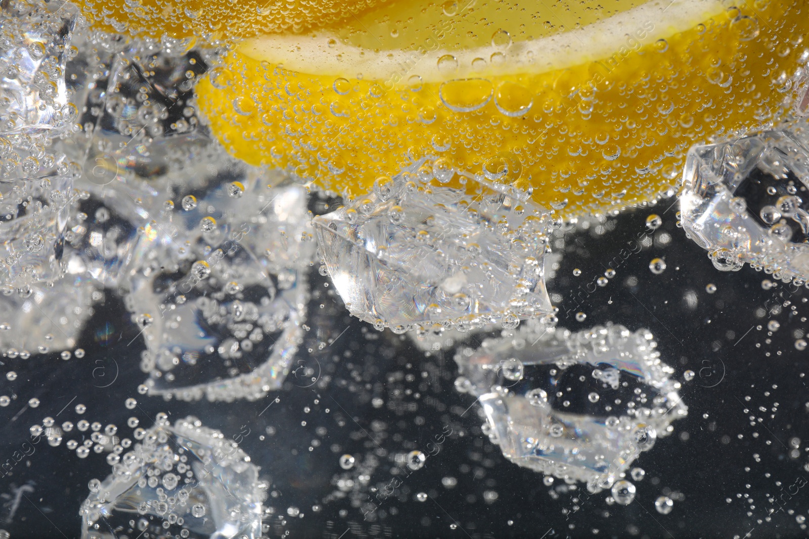 Photo of Juicy lemon slices and ice cubes in soda water against black background, closeup. Space for text