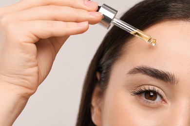 Young woman applying essential oil onto face on light grey background, closeup