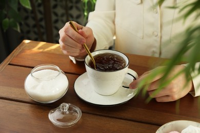 Photo of Woman stirring sugar in tea at wooden table indoors, closeup