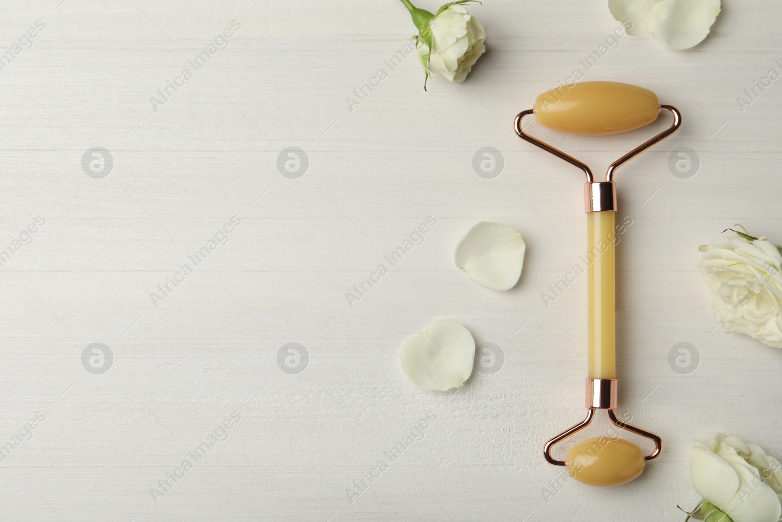 Photo of Natural jade face roller and flowers on white wooden background, flat lay. Space for text
