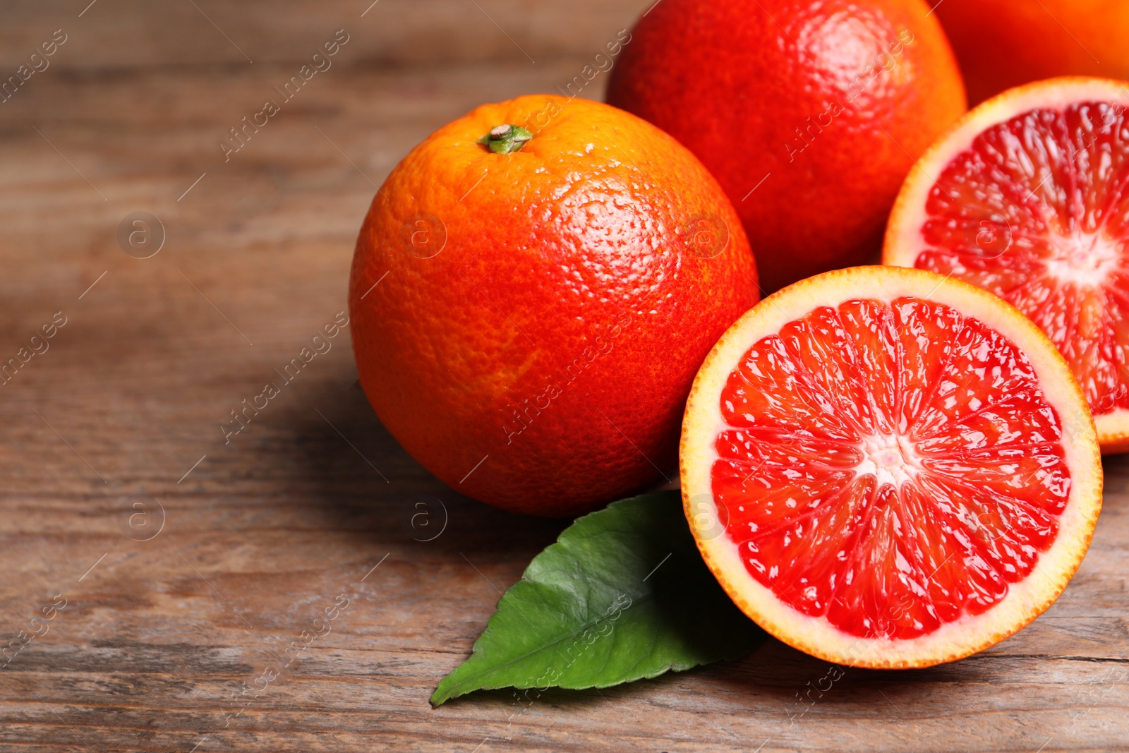 Photo of Whole and cut red oranges on wooden table, closeup