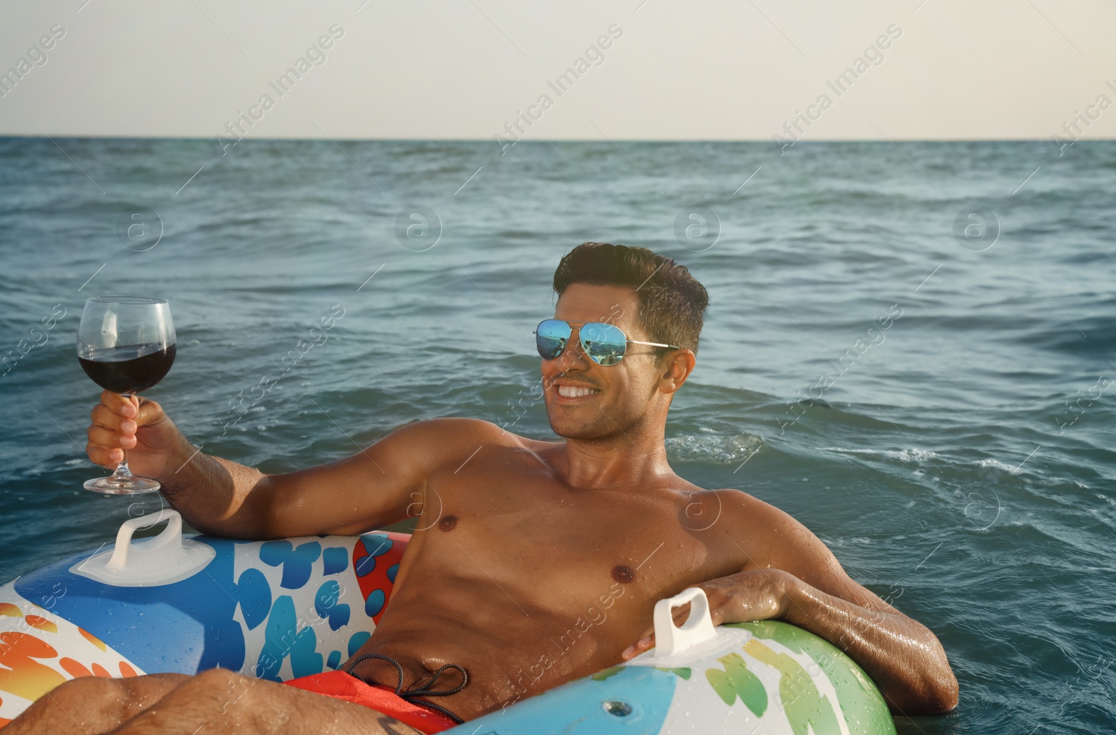 Photo of Man with glass of wine and inflatable ring resting in sea