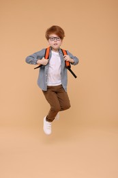 Photo of Cute schoolboy with backpack jumping on beige background