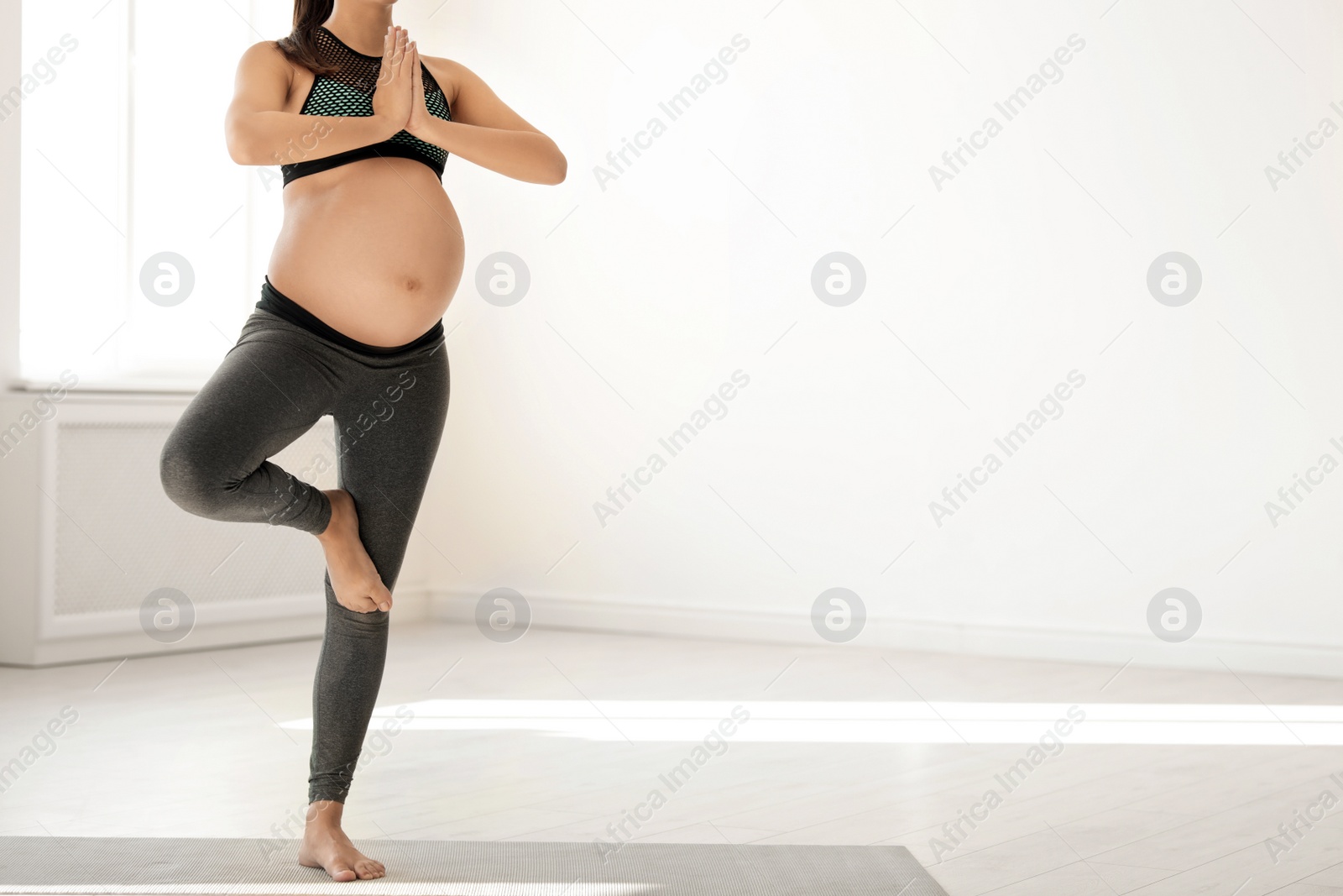 Photo of Young pregnant woman in fitness clothes practicing yoga at home. Space for text