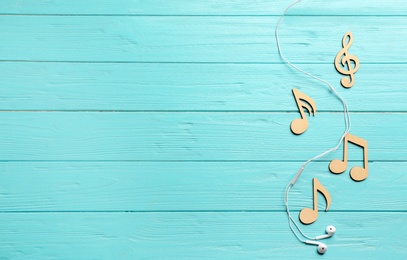Photo of Flat lay composition with music notes, earphones and space for text on color wooden background