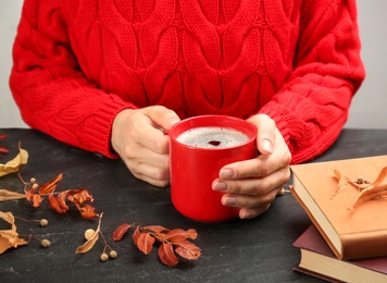 Woman with cup of hot drink at black table, closeup. Cozy autumn atmosphere