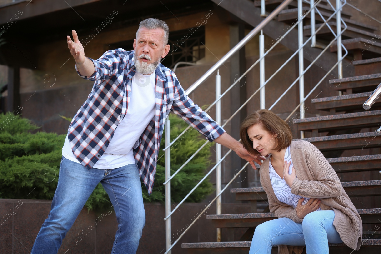 Photo of Man helping mature woman having heart attack on stairs, outdoors