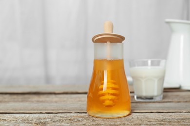 Jar with honey and glass of milk on wooden table. Space for text