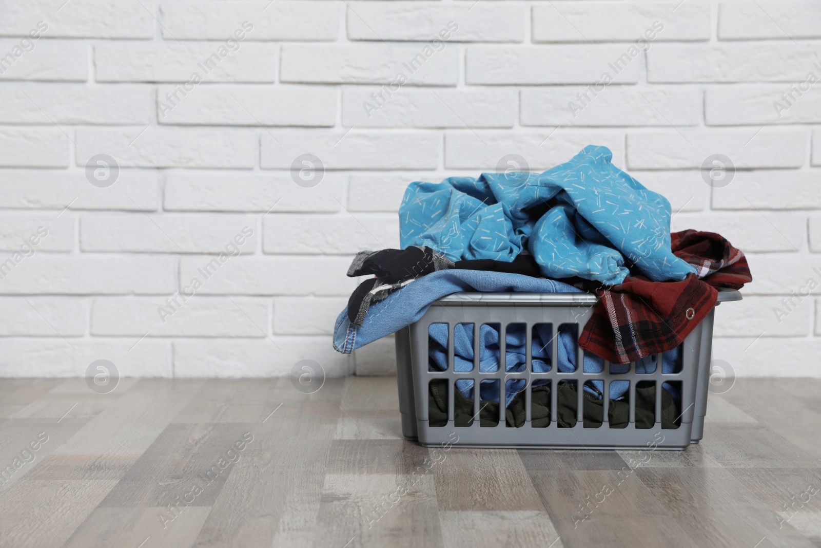 Photo of Laundry basket with dirty clothes on floor near brick wall. Space for text