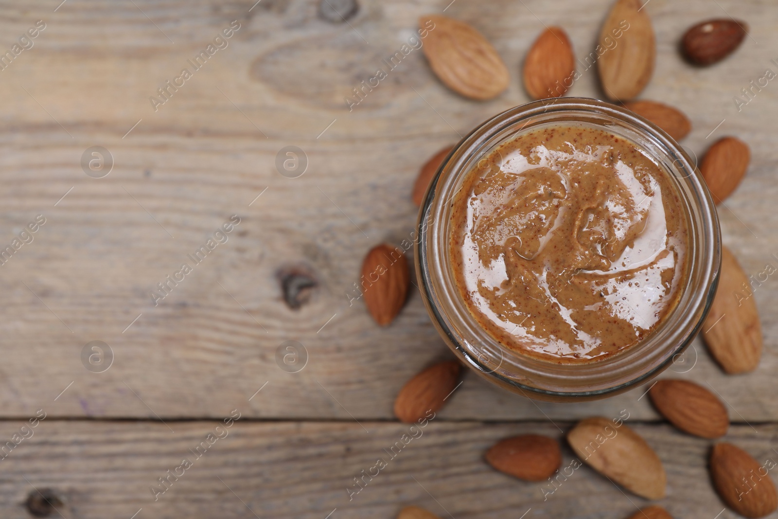 Photo of Tasty almond nut paste in jar on wooden table, top view. Space for text