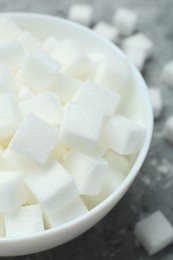 Photo of White sugar cubes in bowl on grey table, closeup