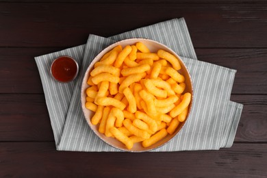 Photo of Crunchy cheesy corn snack in bowl and ketchup on wooden table, flat lay