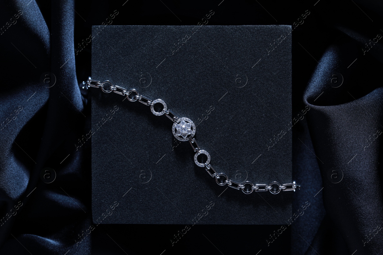 Photo of Elegant jewelry. Stylish presentation of luxury bracelet on dark blue podium, top view