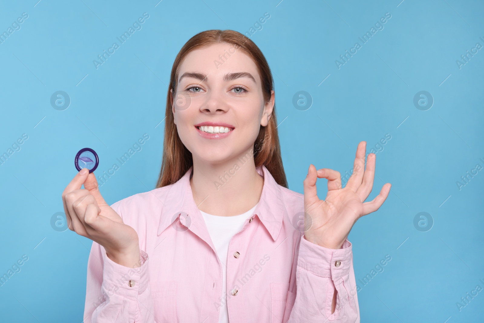 Photo of Woman with condom showing ok gesture on turquoise background. Safe sex