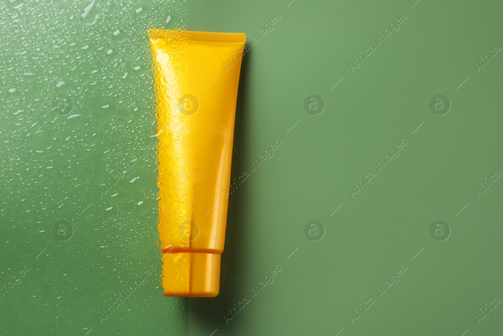 Photo of Tube with moisturizing cream on wet green surface, top view. Space for text