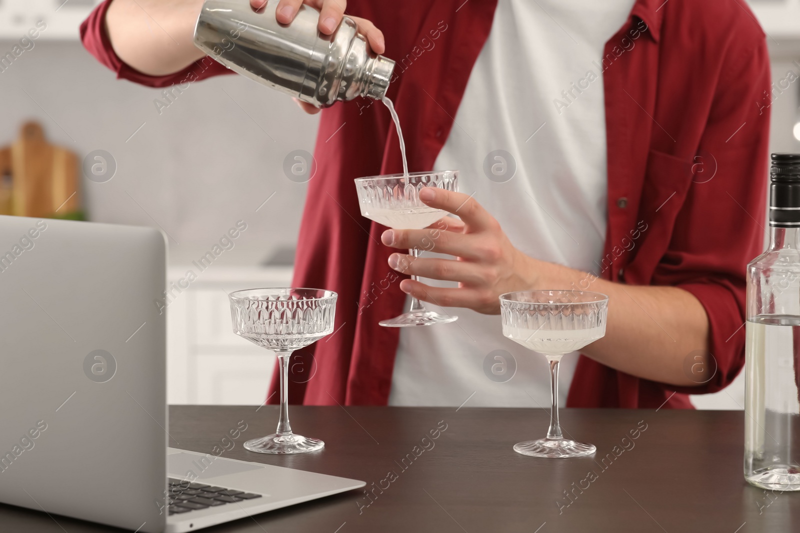 Photo of Man learning to make cocktail with online video on laptop at wooden table in kitchen, closeup. Time for hobby