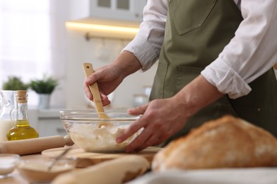 Photo of Making bread. Man preparing dough in bowl at wooden table in kitchen, closeup