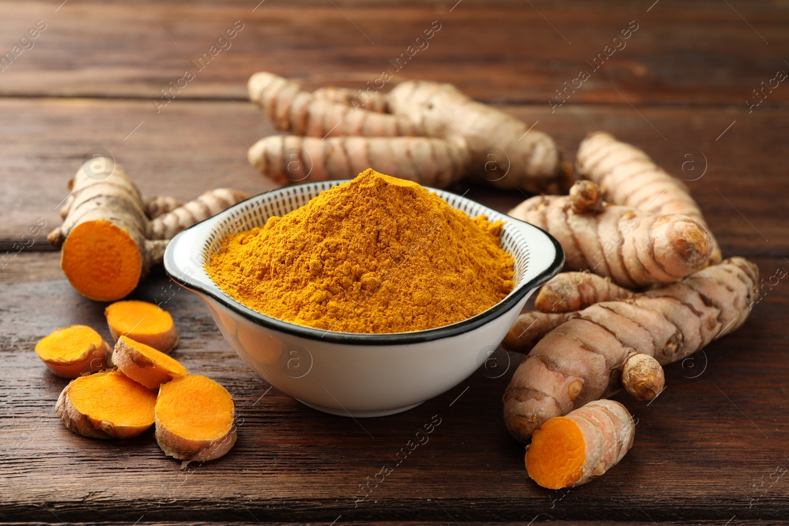 Photo of Bowl with aromatic turmeric powder and cut roots on wooden table