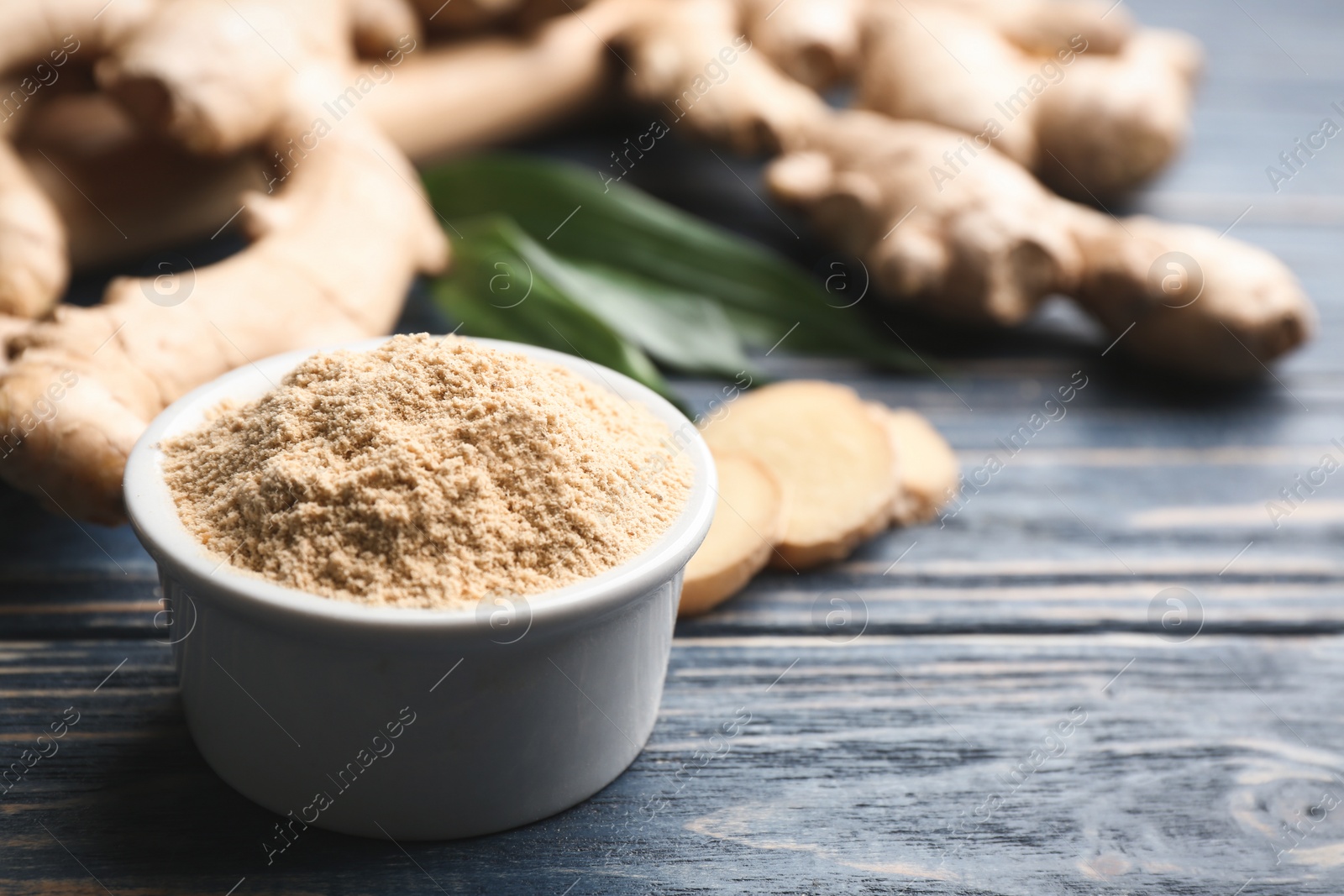 Photo of Dry ginger powder in bowl and fresh root on blue wooden table. Space for text