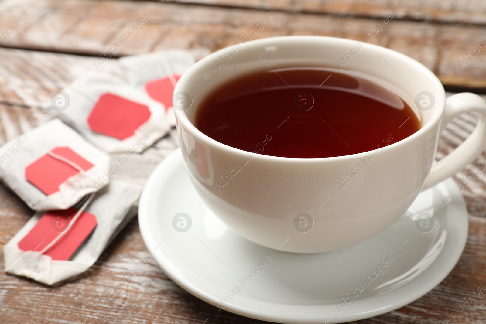 Photo of Tea bags and cup of aromatic drink on wooden rustic table, closeup