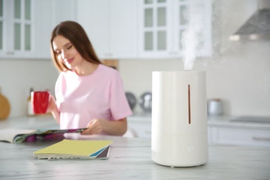 Modern air humidifier and blurred woman drinking coffee in kitchen