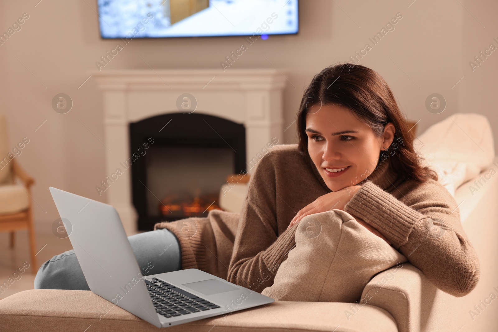 Photo of Young woman with laptop on sofa near fireplace at home