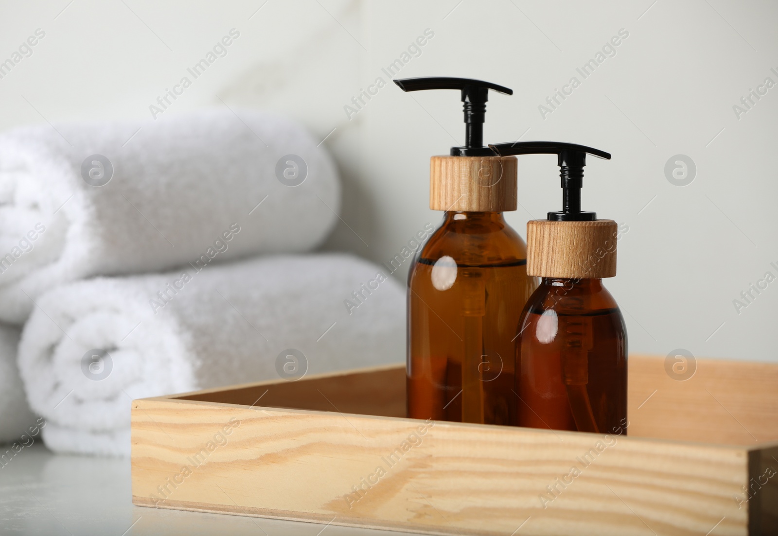 Photo of Wooden tray with dispenser bottles and towels on white table, closeup