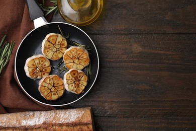 Frying pan with fried garlic, rosemary, oil and bread on wooden table, flat lay. Space for text