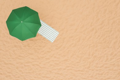 Green beach umbrella and towel on sandy coast, aerial view. Space for text