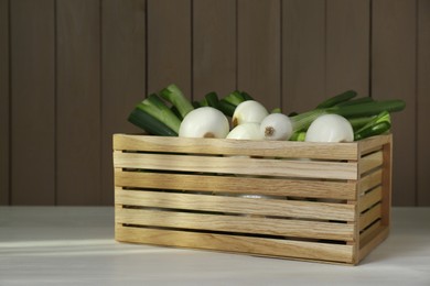Crate with green spring onions on white wooden table