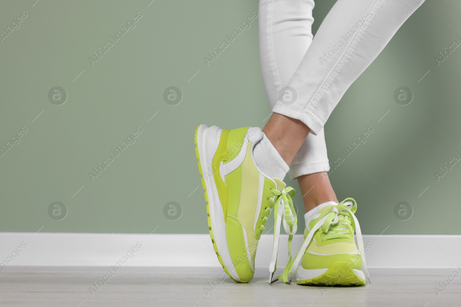 Photo of Woman wearing new stylish sneakers near light green wall, closeup. Space for text